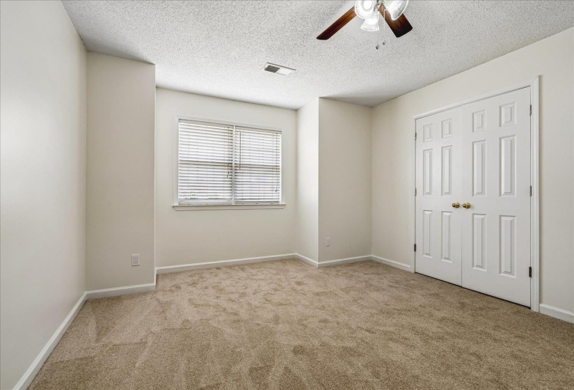 Carpeted room featuring a window with blinds, a ceiling fan, and bi-fold closet doors