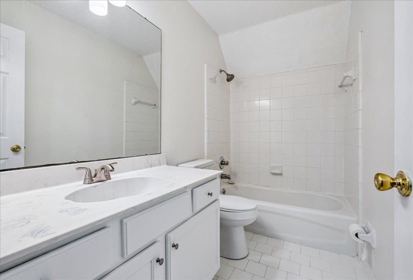 Bathroom featuring a white vanity with an integrated sink, a large mirror, a white tiled tub/shower combination, and white floor tiling