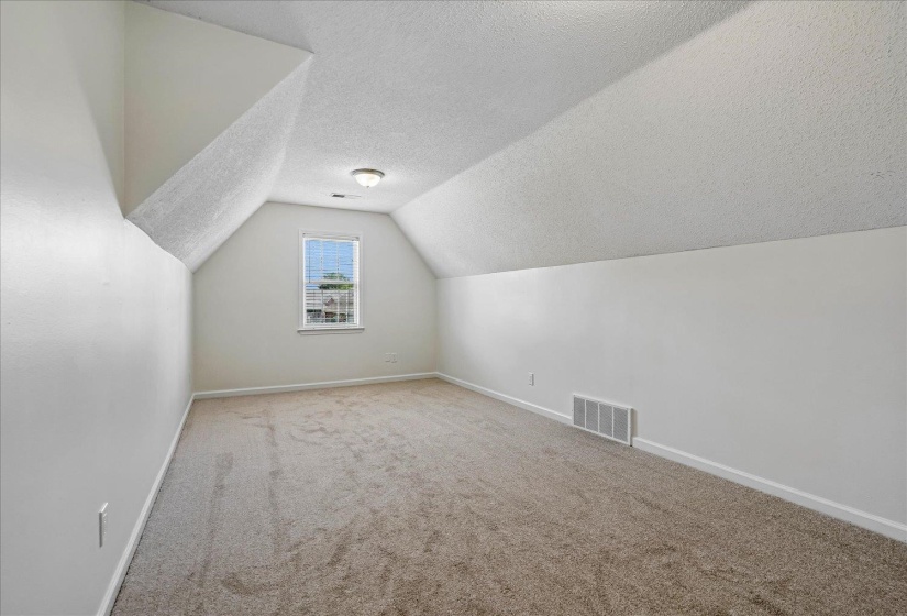 Carpeted room featuring a single window with blinds, sloped ceilings, and a flush mount light fixture