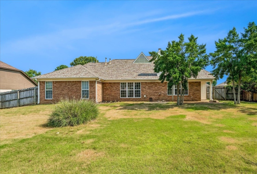 Rear exterior featuring brick siding, a gabled roofline, multiple windows, an outdoor patio, and mature trees