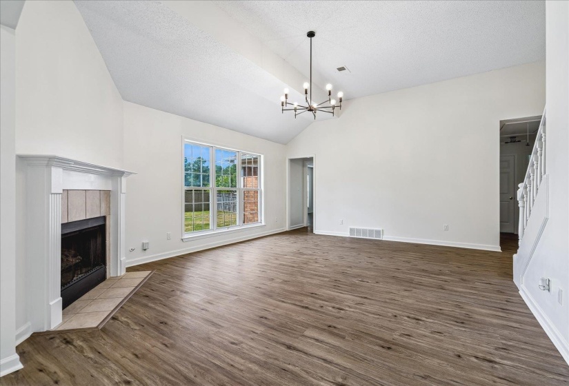 Spacious interior featuring vaulted ceilings, a central fireplace with tile surround, large windows, wood-finish flooring, and a contemporary chandelier