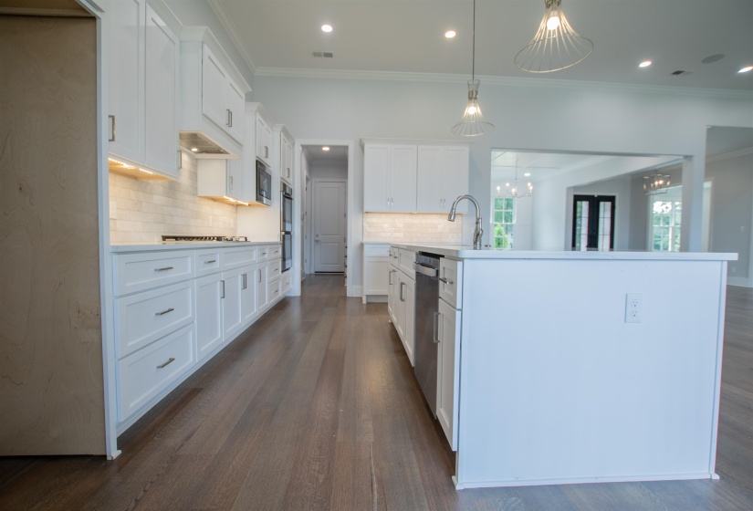 Kitchen with tasteful backsplash, white cabinets, dark hardwood / wood-style flooring, a kitchen island with sink, and hanging light fixtures