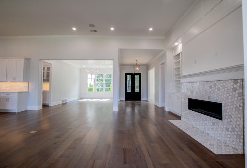 Unfurnished living room featuring built in features, an inviting chandelier, crown molding, a tiled fireplace, and dark wood-type flooring