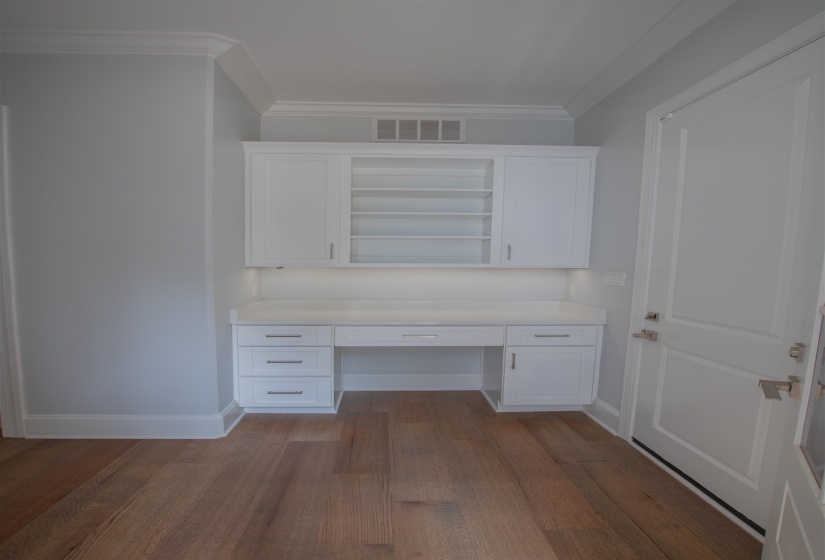 Unfurnished office with built in desk, hardwood / wood-style floors, and ornamental molding