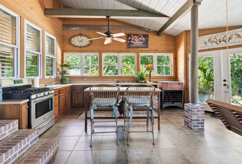 Kitchen featuring vaulted ceiling with beams, wooden walls, tile patterned flooring, stainless steel gas range oven, and ceiling fan