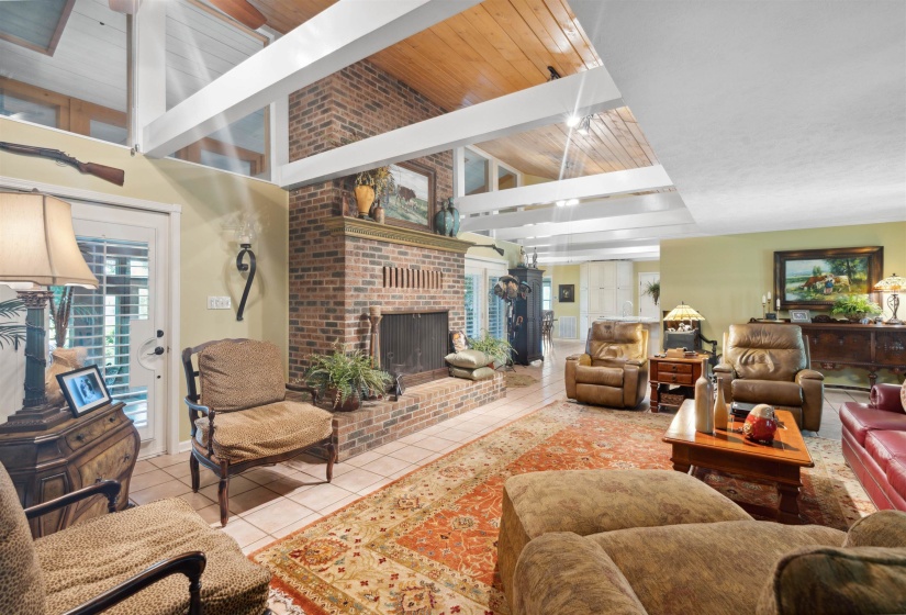 Tiled living room with brick wall, a fireplace, lofted ceiling with beams, and wood ceiling