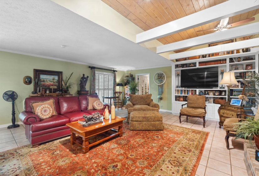 Tiled living room featuring beamed ceiling, built in features, wood ceiling, and ceiling fan