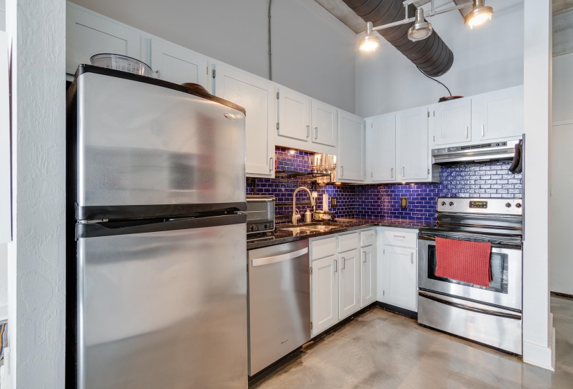 Kitchen featuring dark stone counters, stainless steel appliances, white cabinets, sink, and backsplash