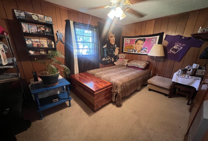 Bedroom featuring carpet flooring, a textured ceiling, wood walls, and ceiling fan