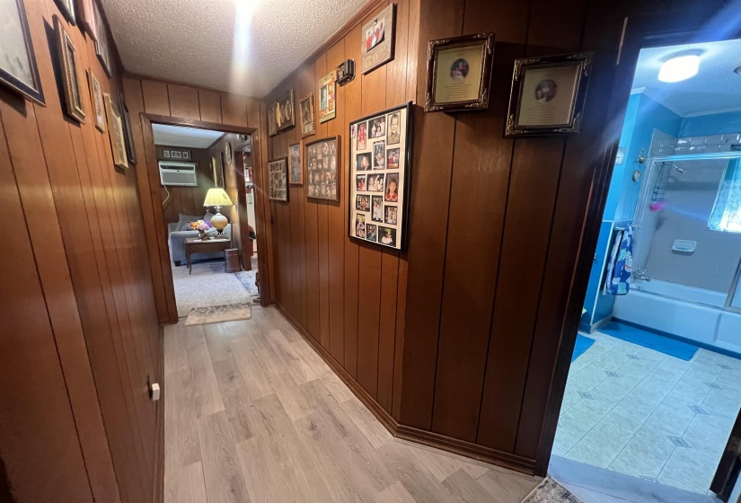 Hallway featuring an AC wall unit, wooden walls, light wood-type flooring, and a textured ceiling