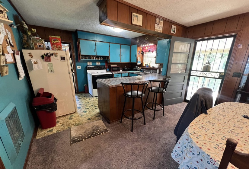 Kitchen featuring white appliances, a textured ceiling, kitchen peninsula, wood walls, and carpet