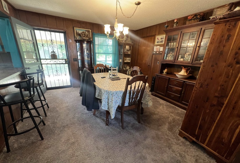 Carpeted dining area with a textured ceiling, wood walls, and an inviting chandelier