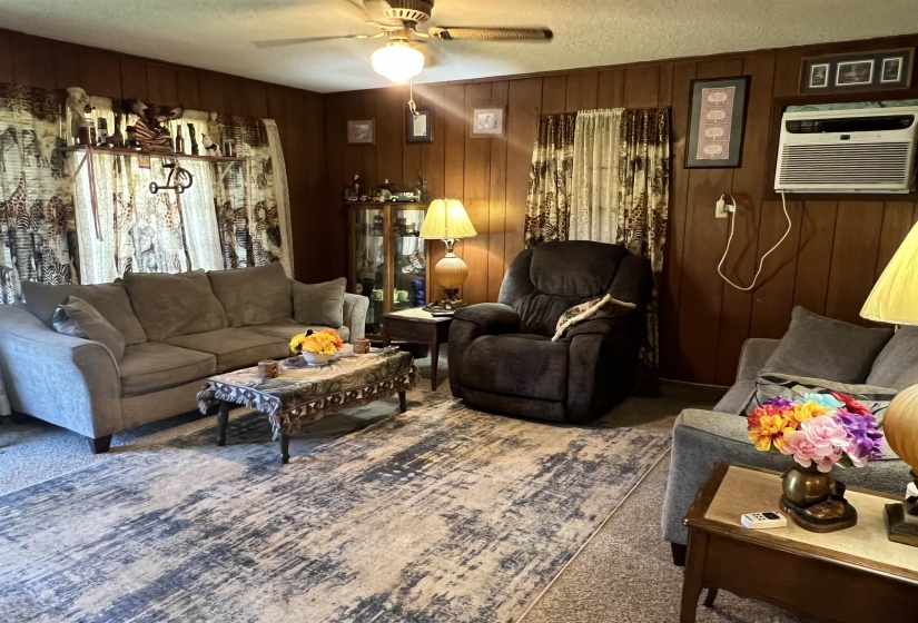 Carpeted living room featuring an AC wall unit, a textured ceiling, ceiling fan, and wooden walls