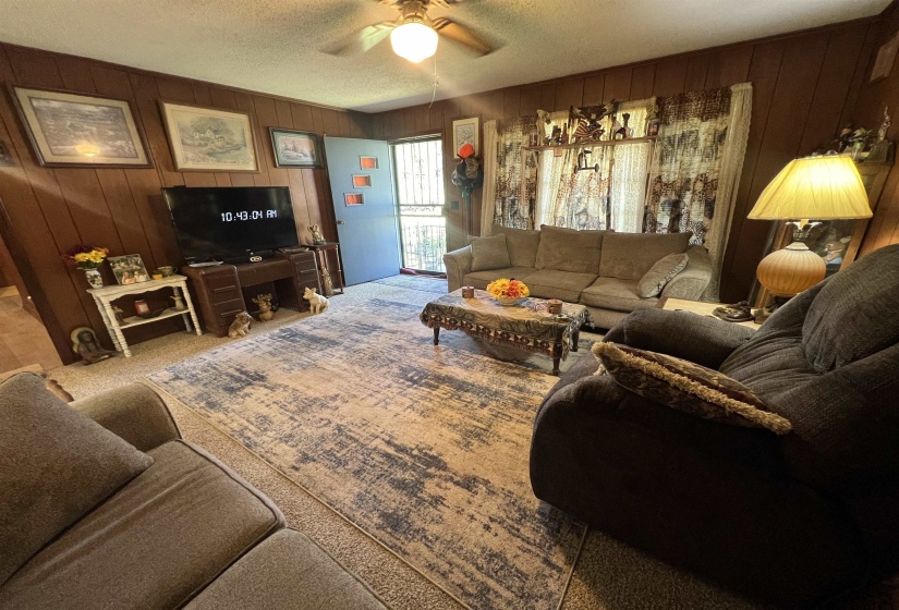 Living room with wood walls, carpet, ceiling fan, and a textured ceiling