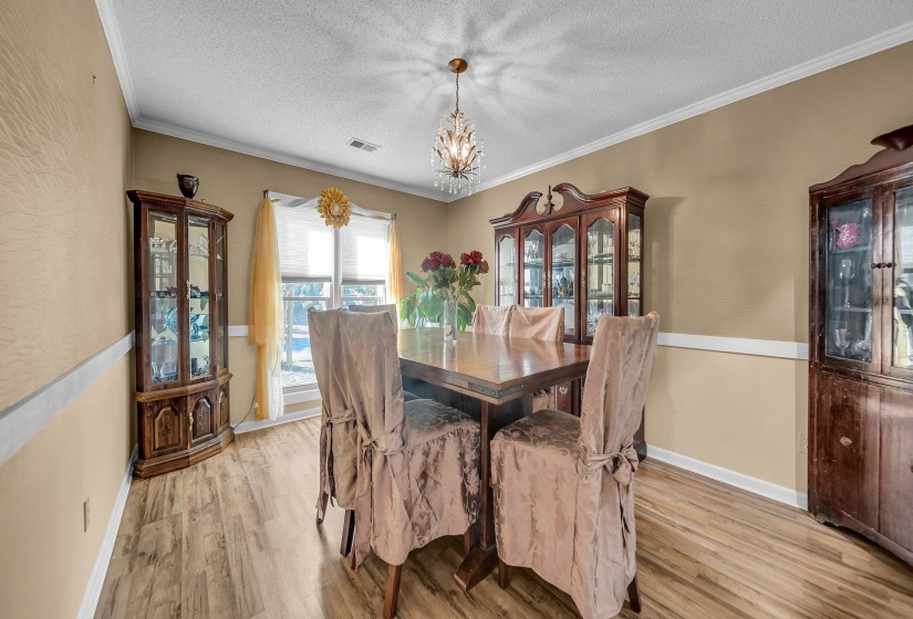 Dining area with light hardwood / wood-style flooring, a textured ceiling, a notable chandelier, and crown molding