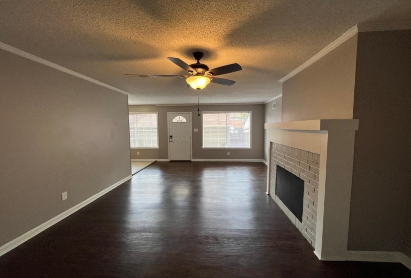 Unfurnished living room with ceiling fan, a fireplace, dark wood-type flooring, and ornamental molding