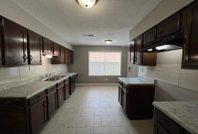 Kitchen with a textured ceiling, dark brown cabinets, decorative backsplash, and light tile patterned floors