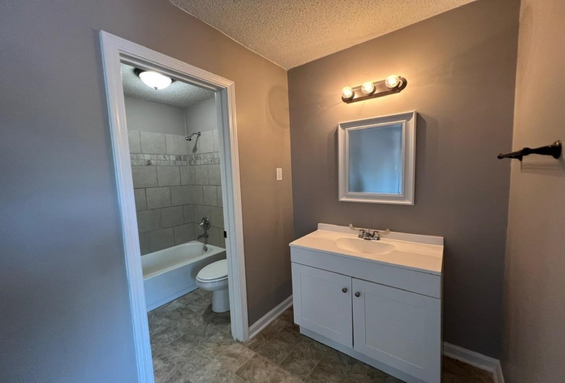 Full bathroom featuring a textured ceiling, tiled shower / bath, toilet, vanity, and tile patterned floors