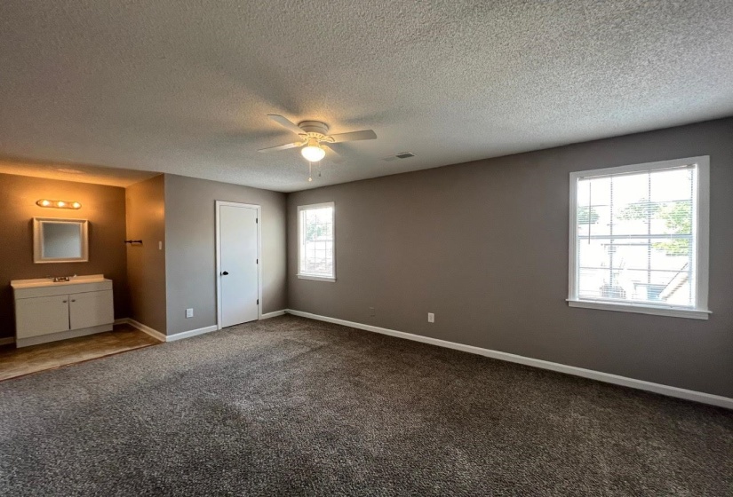 Unfurnished bedroom with multiple windows, a textured ceiling, connected bathroom, and carpet flooring