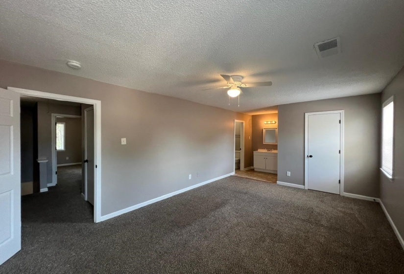 Unfurnished bedroom with ensuite bath, a textured ceiling, ceiling fan, and carpet flooring