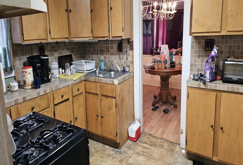 Kitchen featuring gas stove, an inviting chandelier, tile countertops, sink, and tasteful backsplash