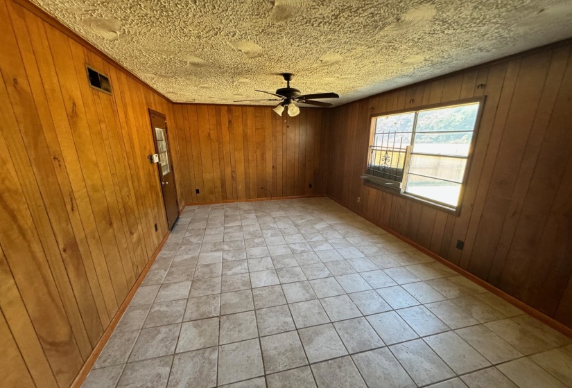 Empty room with wood walls, ceiling fan, light tile patterned flooring, and a textured ceiling