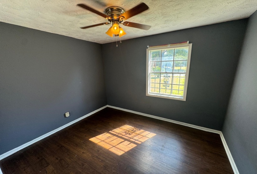 Empty room with ceiling fan, dark wood-type flooring, and a textured ceiling