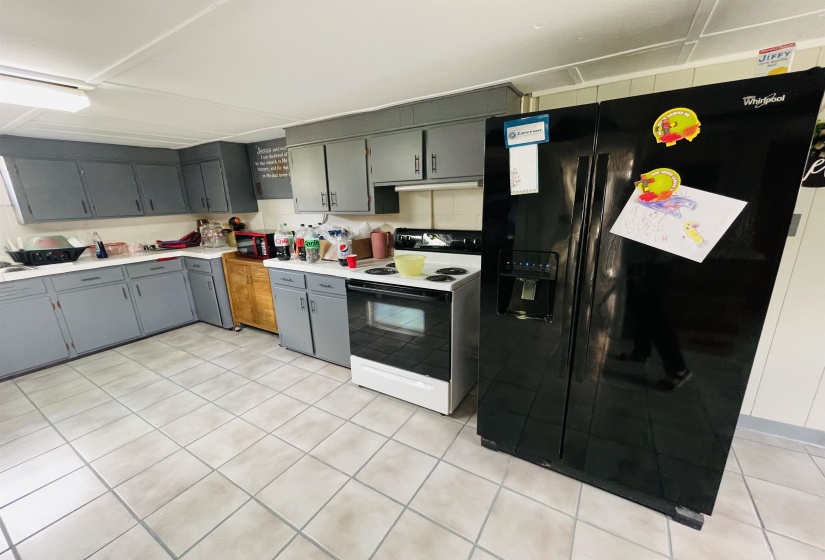 Kitchen with gray cabinets, electric stove, light tile patterned floors, and black refrigerator with ice dispenser