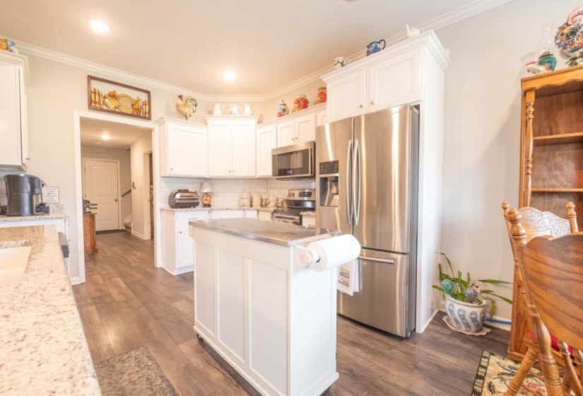 Kitchen with dark hardwood / wood-style floors, white cabinetry, stainless steel appliances, crown molding, and light stone countertops