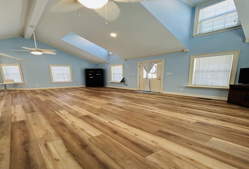 Unfurnished living room featuring high vaulted ceiling, a skylight, wood finished floors, and beam ceiling