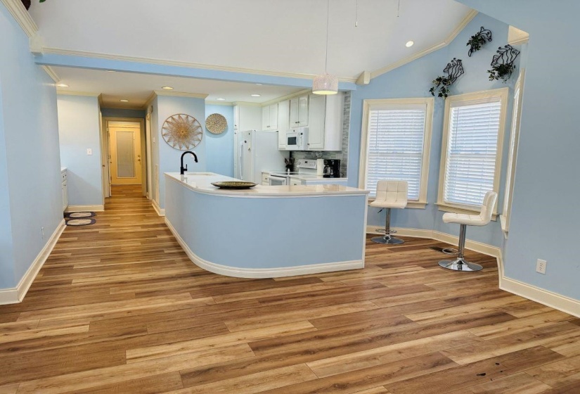 Kitchen featuring white appliances, white cabinetry, vaulted ceiling, and light wood-style flooring