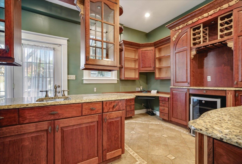 Kitchen with built in desk, sink, wine cooler, and light stone counters