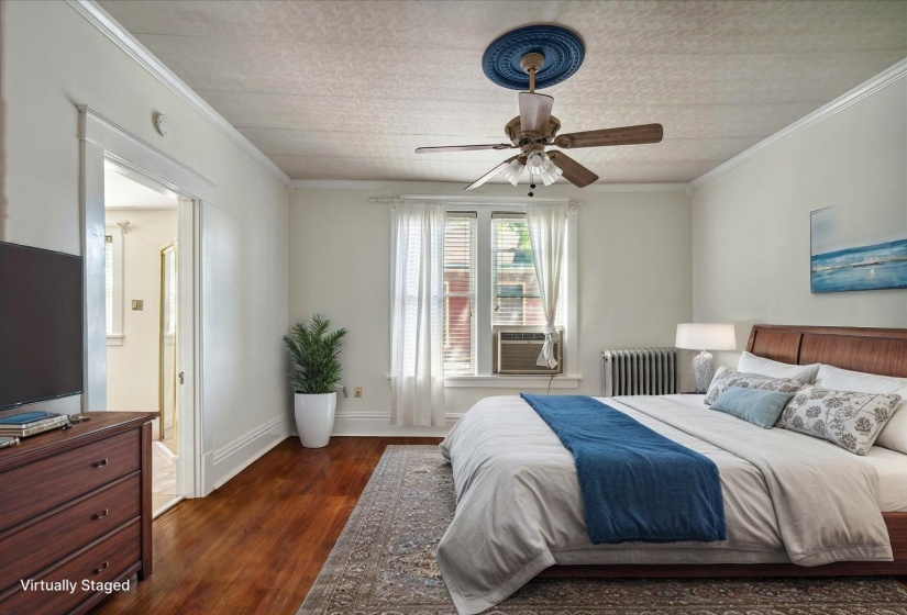 Bedroom with radiator, dark wood finished floors, ornamental molding, ensuite bathroom, and ceiling fan