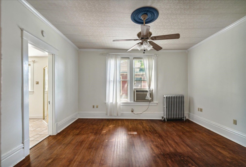 Empty room featuring radiator, ceiling fan, crown molding, and dark hardwood / wood-style floors