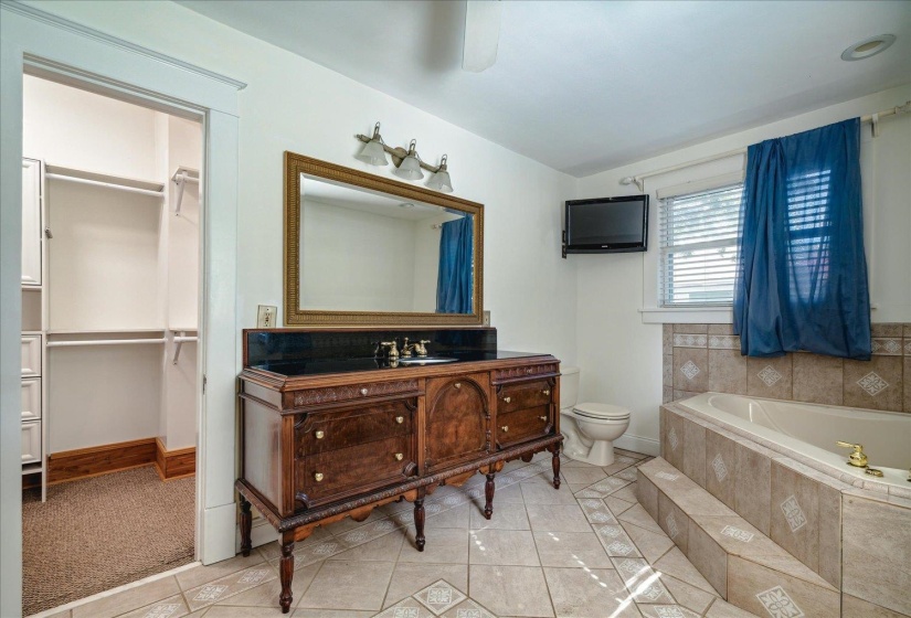 Bathroom featuring toilet, a relaxing tiled tub, vanity, and tile patterned floors