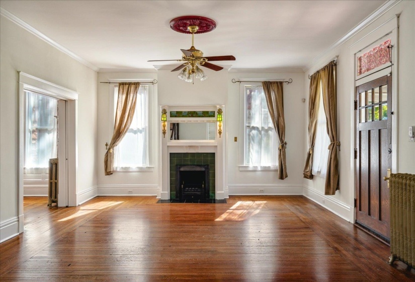 Unfurnished living room with radiator heating unit, ceiling fan, hardwood / wood-style flooring, a tile fireplace, and crown molding