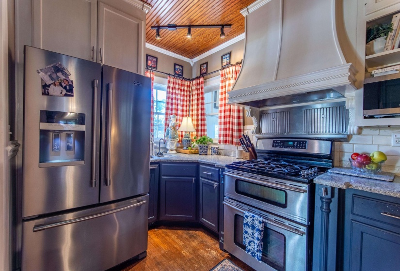 Kitchen with premium range hood, wood ceiling, appliances with stainless steel finishes, crown molding, and light hardwood / wood-style floors