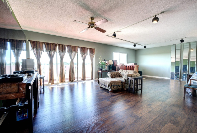 Living room featuring a textured ceiling, rail lighting, ceiling fan, and dark wood-type flooring