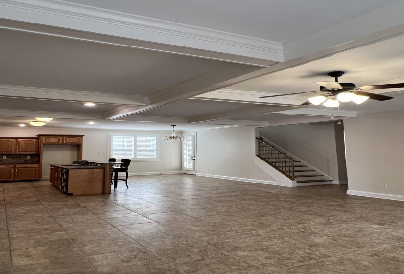Unfurnished living room featuring coffered ceiling, ceiling fan with notable chandelier, sink, ornamental molding, and beamed ceiling