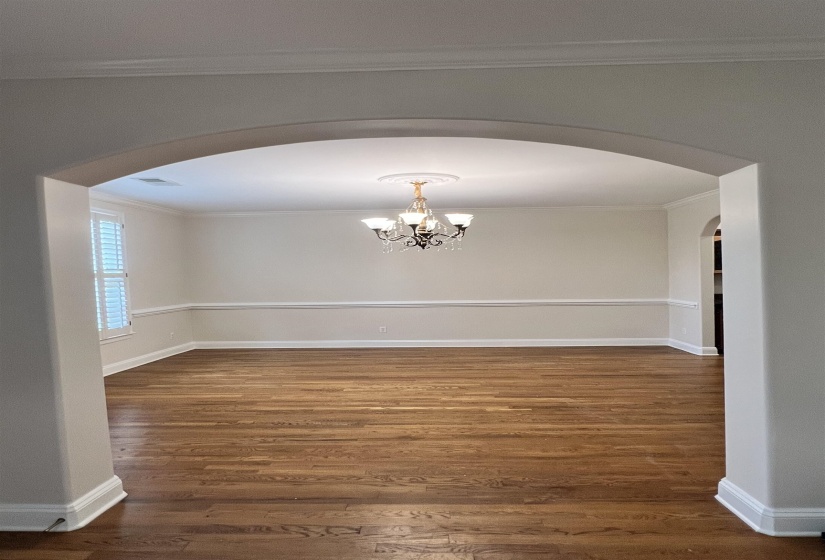 Empty room with ornamental molding, dark wood-type flooring, and an inviting chandelier