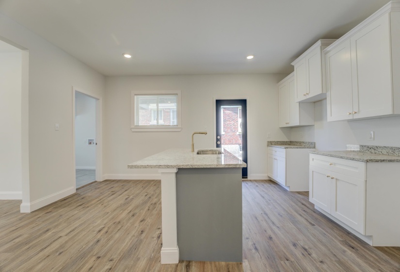 Kitchen featuring a center island with sink, light hardwood / wood-style floors, light stone counters, sink, and white cabinets