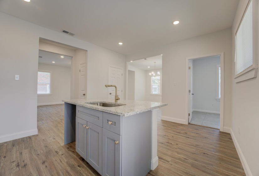 Kitchen with an island with sink, light stone countertops, gray cabinetry, sink, and hardwood / wood-style floors