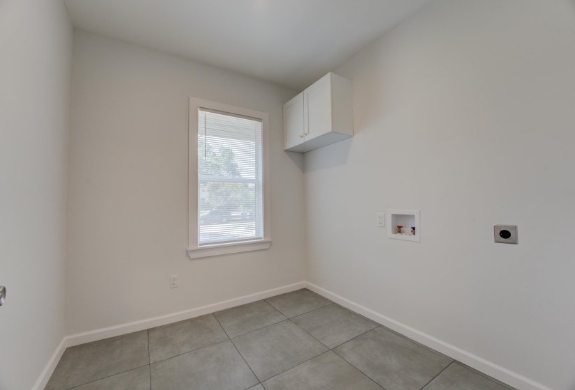 Washroom with hookup for a washing machine, cabinets, light tile patterned floors, and electric dryer hookup