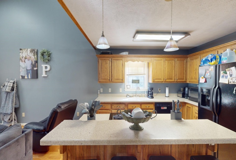 Kitchen with black refrigerator with ice dispenser, a textured ceiling, decorative light fixtures, and a breakfast bar area