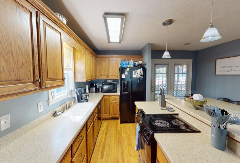 Kitchen featuring black appliances, hanging light fixtures, light wood-type flooring, and a healthy amount of sunlight