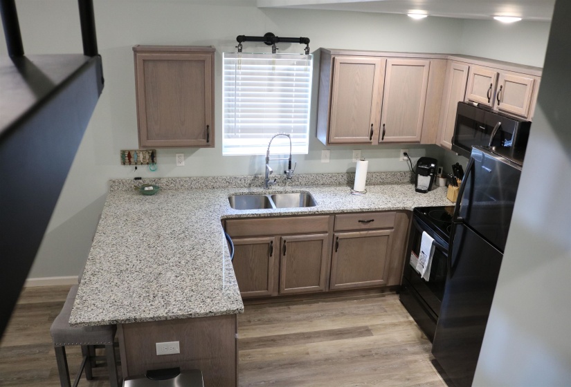 Kitchen with black appliances, light wood-type flooring, light stone countertops, sink, and a kitchen breakfast bar