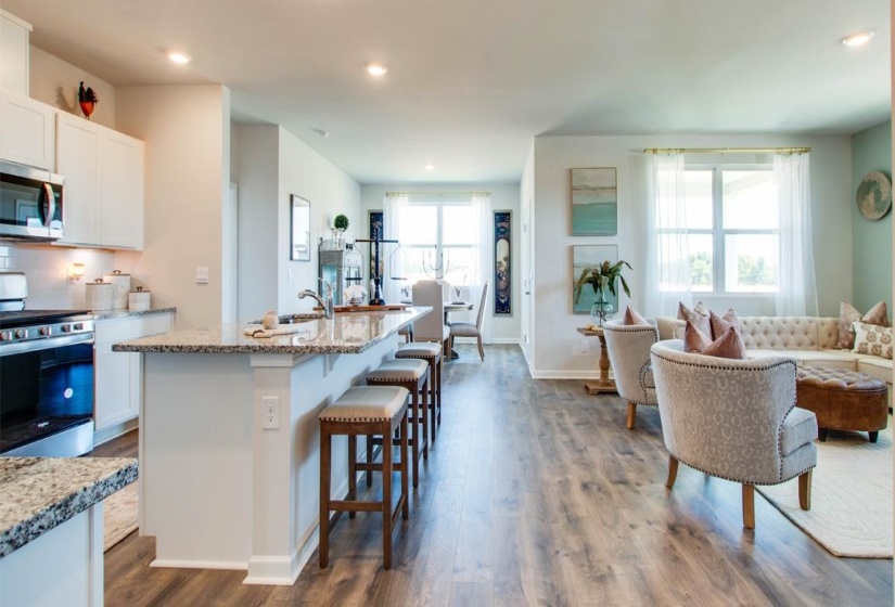 Kitchen with white cabinets, appliances with stainless steel finishes, light stone counters, and an island with sink