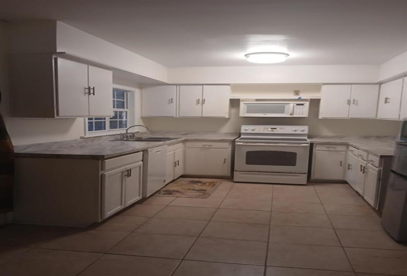 Kitchen with light tile patterned flooring, white appliances, white cabinetry, and sink