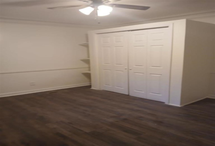 Unfurnished bedroom featuring ceiling fan, crown molding, dark wood-type flooring, and a closet