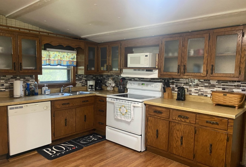 Kitchen featuring white appliances, under cabinet range hood, backsplash, and lofted ceiling